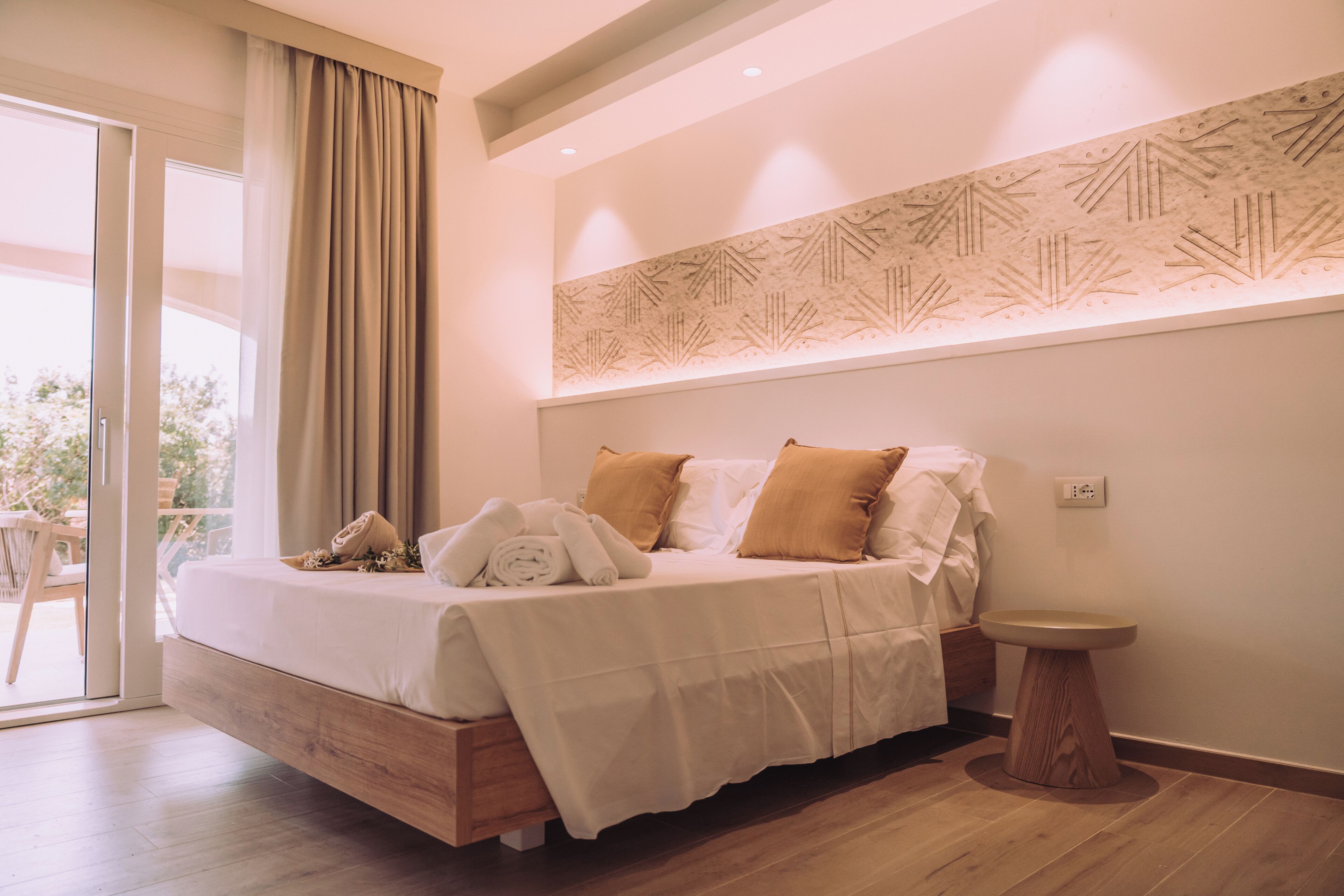 A modern bedroom with a bed, bedside table, and a view through a glass door.