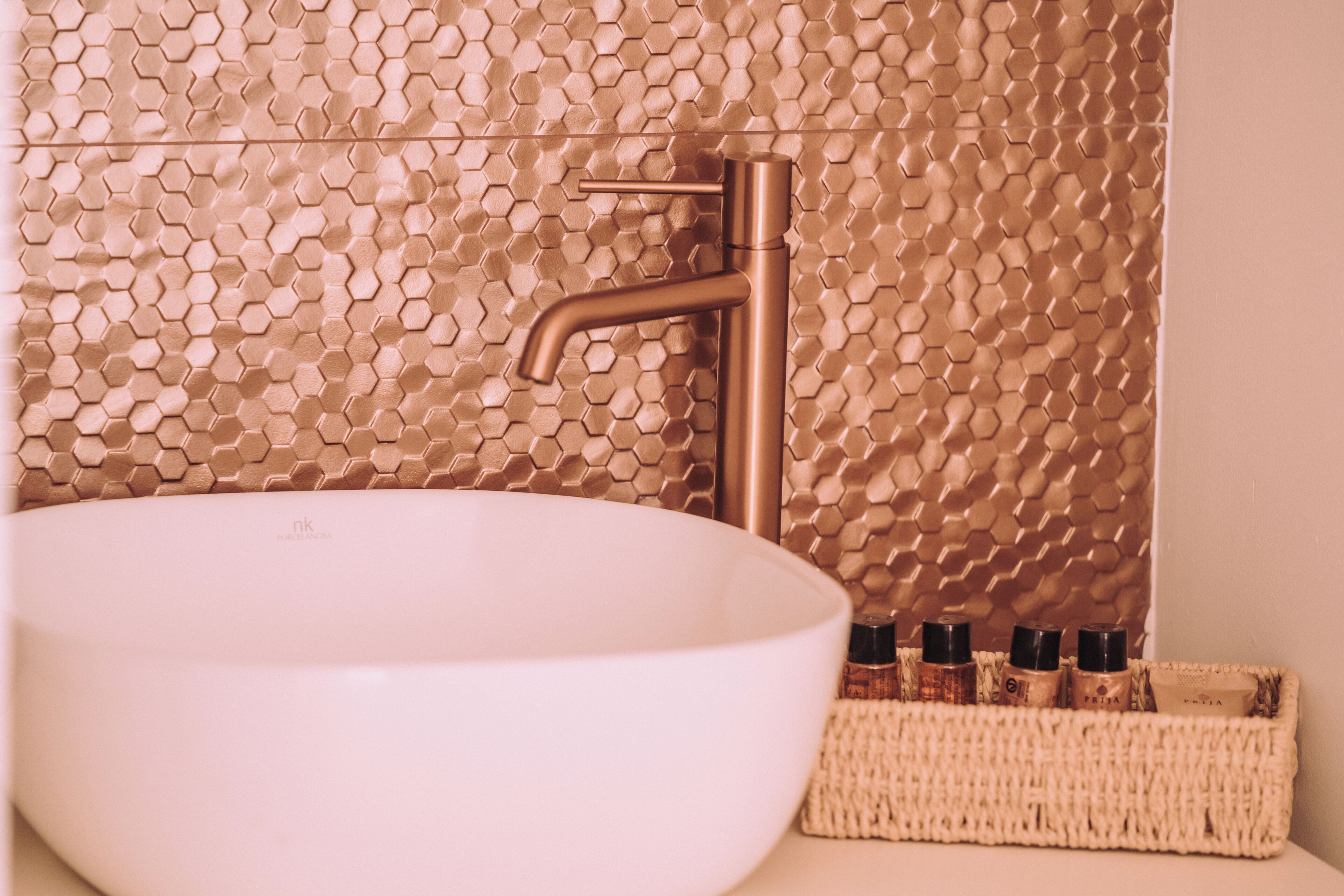 Een badkamer met een wit wastafelmeubel, een wand met een hexagonaal patroon, en een gevlochten mand met toiletartikelen.