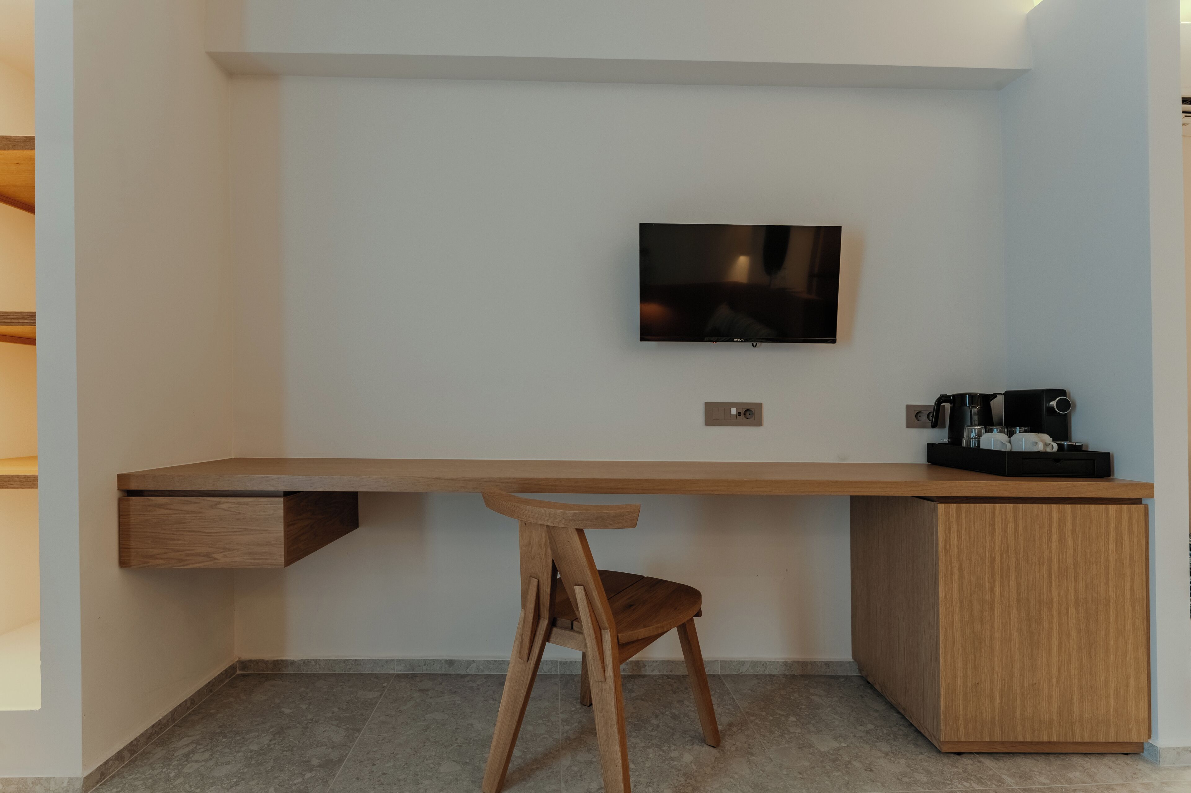 A modern, minimalist room with a wooden desk, a chair, a television, and a coffee machine.