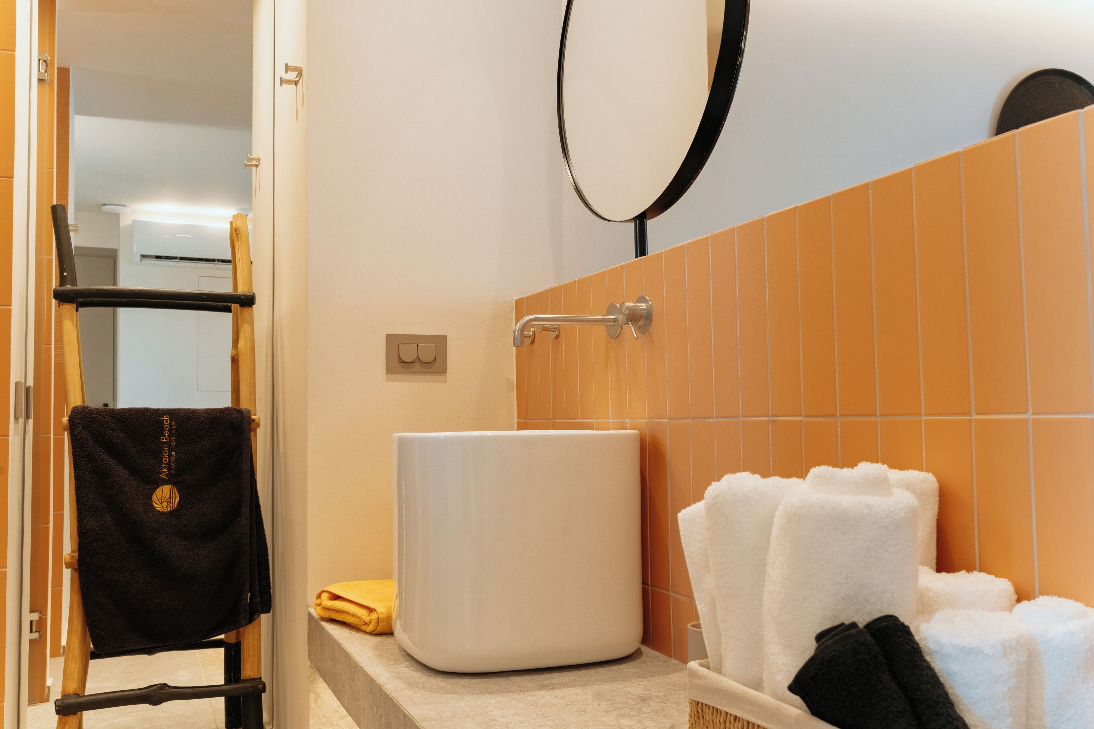 Une salle de bain avec un lavabo blanc, un porte-serviettes sur lequel est posée une serviette noire, et un miroir.