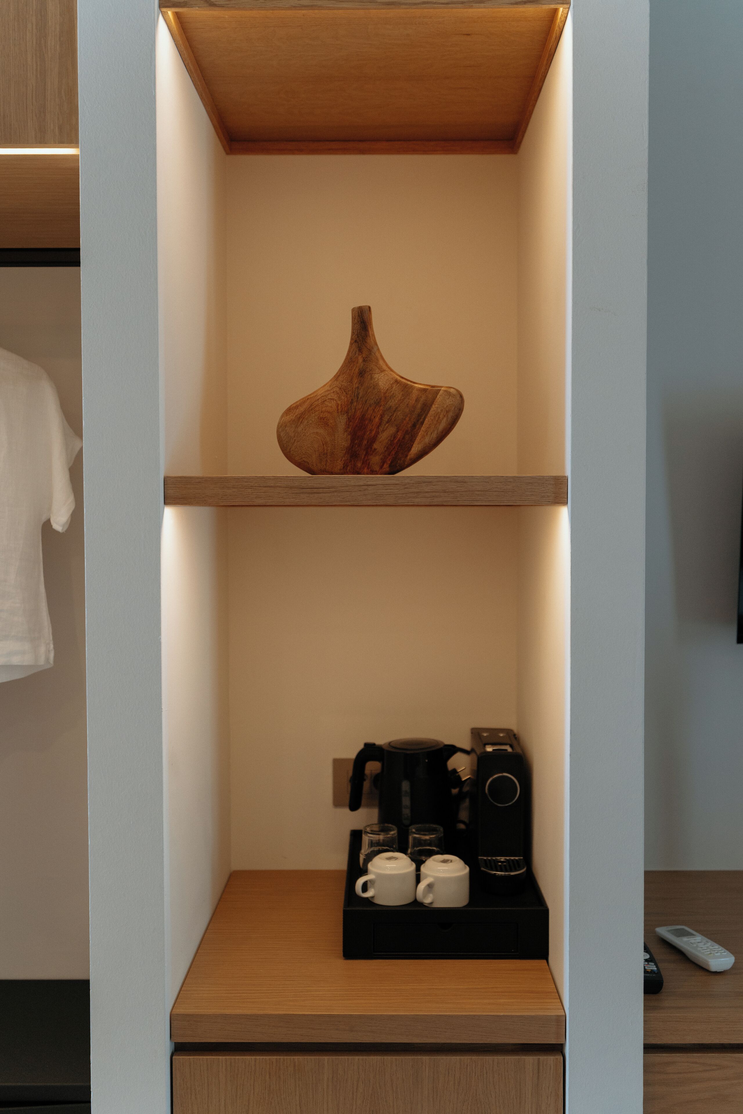 A shelf with a wooden bowl, a coffee maker, and two cups on a wooden surface.