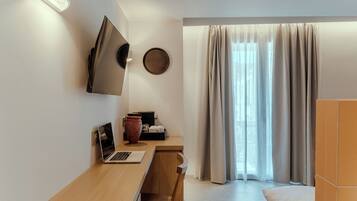 A modern bedroom with a wooden desk, a laptop, a vase, and a bed.