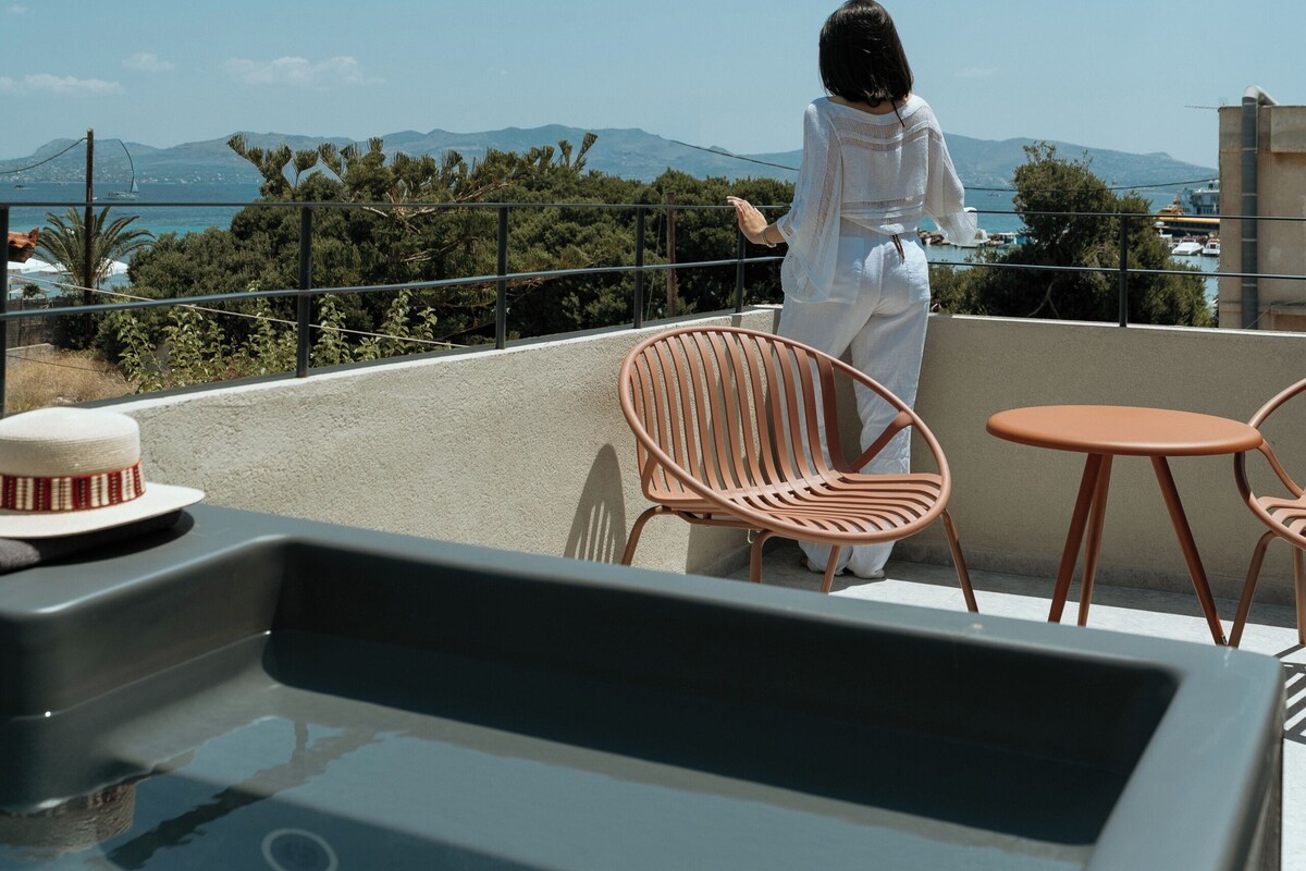 Una persona sentada en una silla contemplando una vista panorámica con montañas y una masa de agua al fondo.