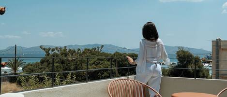 Una persona sentada en una silla contemplando una vista panorámica con montañas y una masa de agua al fondo.