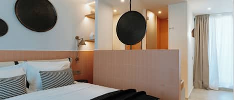 A modern hotel room with a large bed, a bedside table, a mirror, and a view of the bathroom.