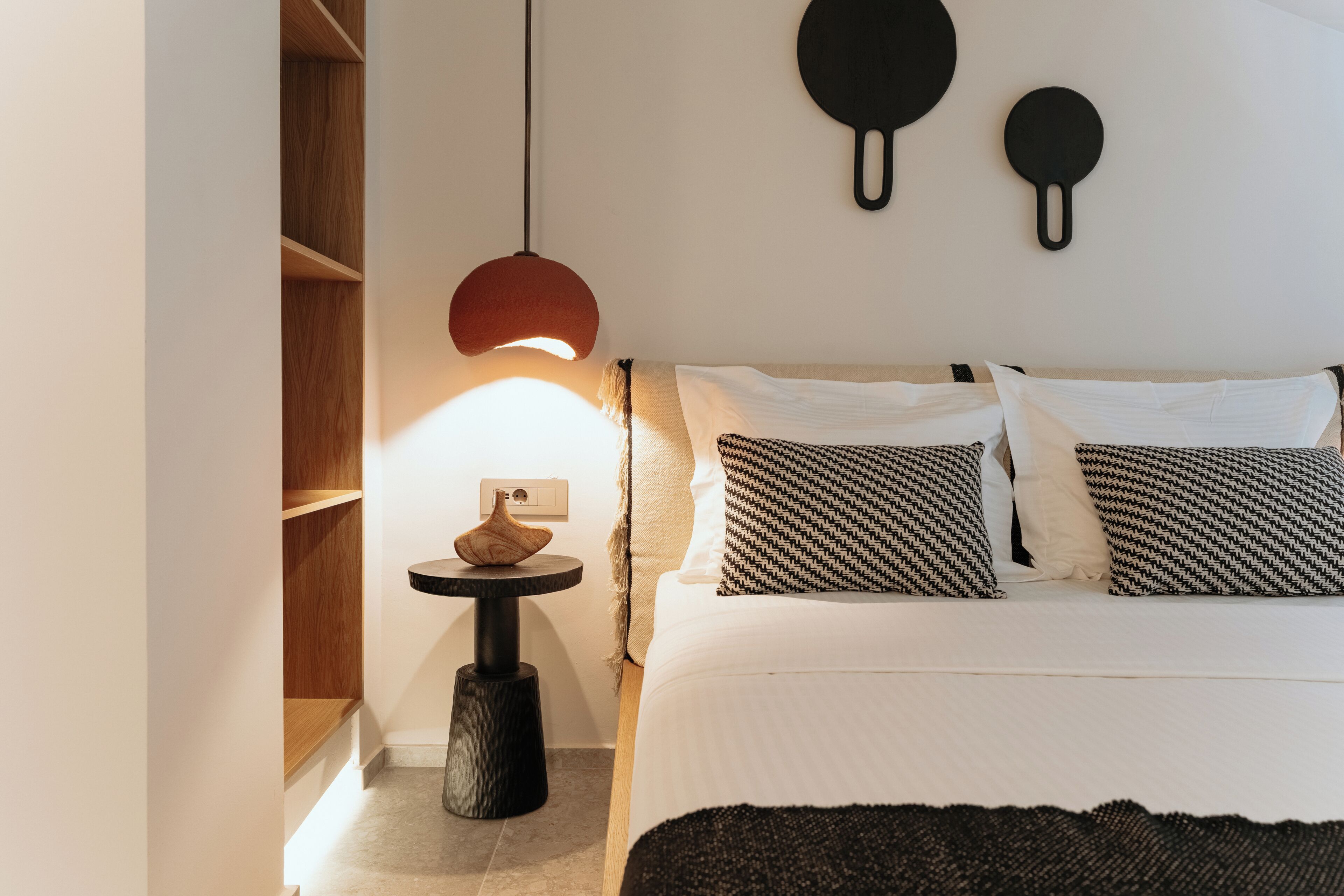 A bedroom with a bed, bedside tables, a hanging light fixture, and a wall-mounted object.