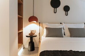 A bedroom with a bed, bedside tables, a hanging light fixture, and a wall-mounted object. - Aktaion Signature Suites (Agistri)