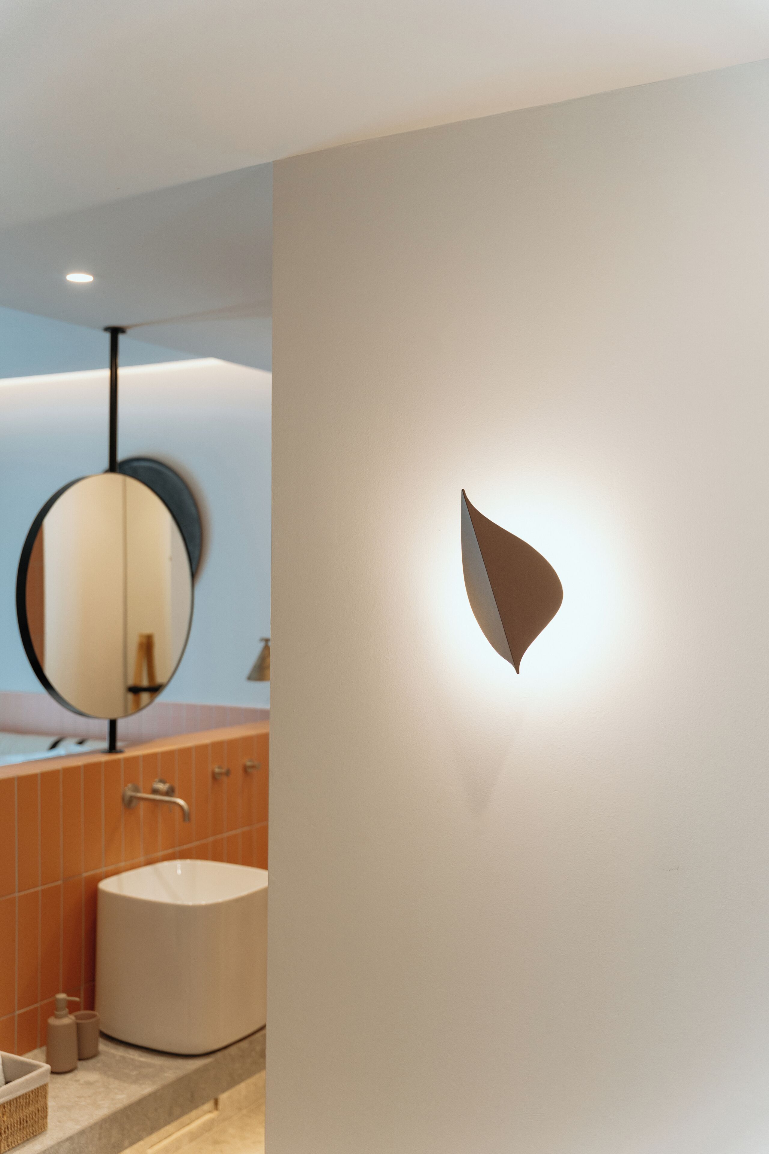 Un baño moderno con un espejo ovalado grande, una lámpara de pared y una bañera independiente.