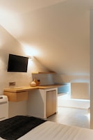 Un dormitorio moderno con techo inclinado, un televisor de pantalla plana montado en la pared, una mesita de noche de madera, una lámpara de noche y una alfombra negra.