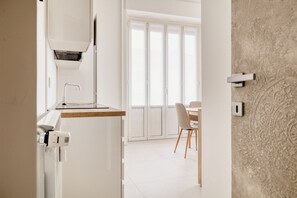 Een moderne keuken met een inbouwoven, een magnetron en een waterdispenser. Er is een eethoek met een tafel en stoelen, en een groot raam met uitzicht op het buiten.