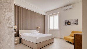 A modern bedroom with a bed, a nightstand, a sofa, a window, and a wall-mounted air conditioner. - Hostmate - Milano - Viale Corsica (Milano)