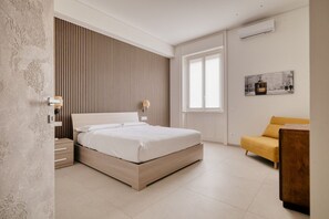 Een moderne slaapkamer met een bed, een nachtkastje, een bank, een raam en een wandairconditioner.