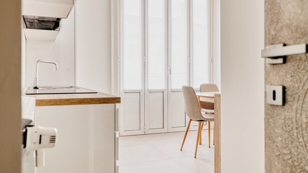 A modern kitchen with a built-in oven, a dining area with a table and chairs, and a large sliding glass door leading to a balcony. - Hostmate - Milano - Viale Corsica (Milano)
