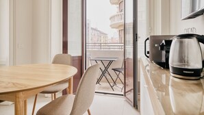 A modern kitchen with a coffee maker, a dining table with chairs, and a balcony with a view of buildings. - Hostmate - Milano - Viale Corsica (Milano)