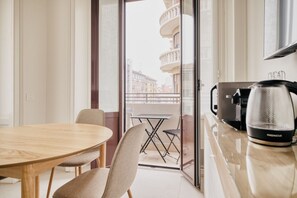 Een moderne keuken met een koffiezetapparaat, een eettafel met stoelen, en een balkon met uitzicht op gebouwen.