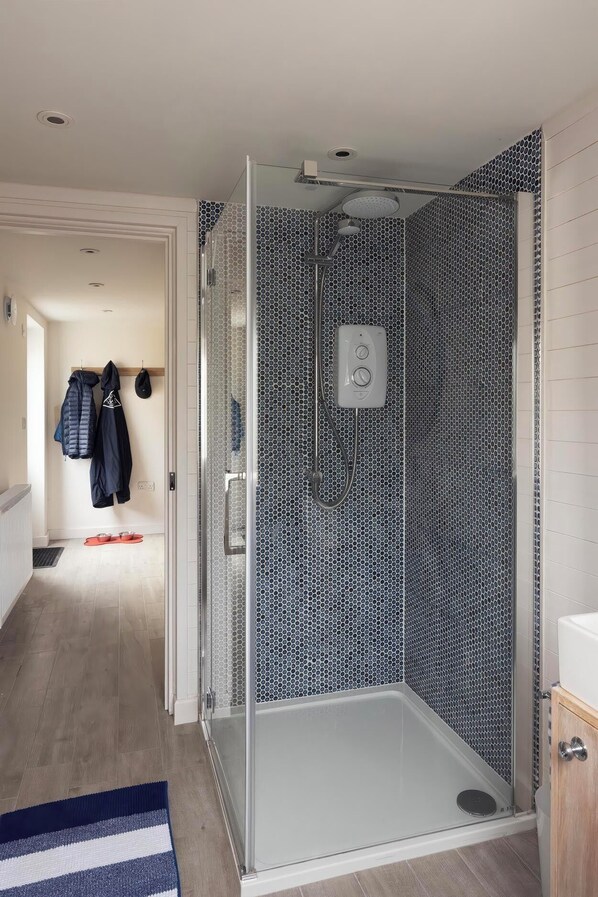 A modern bathroom with a glass shower enclosure, a white sink, and a patterned wall. - Rose Cottage (Wadebridge)