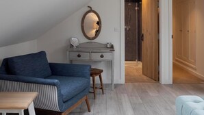 A modern loft bedroom with a skylight, a blue sofa, a wooden desk, and a walk-in closet. - Rose Cottage (Wadebridge)
