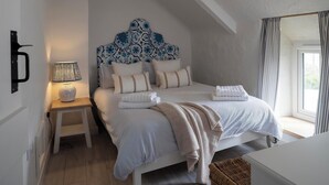 A bedroom with a bed, bedside lamp, and a window with curtains. - Rose Cottage (Wadebridge)
