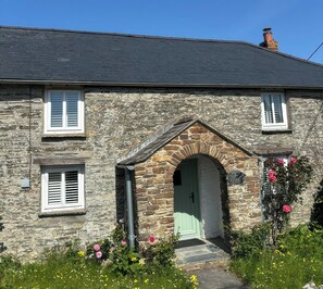 Una casa de piedra con un arco de entrada central, dos ventanas con contraventanas y una chimenea.