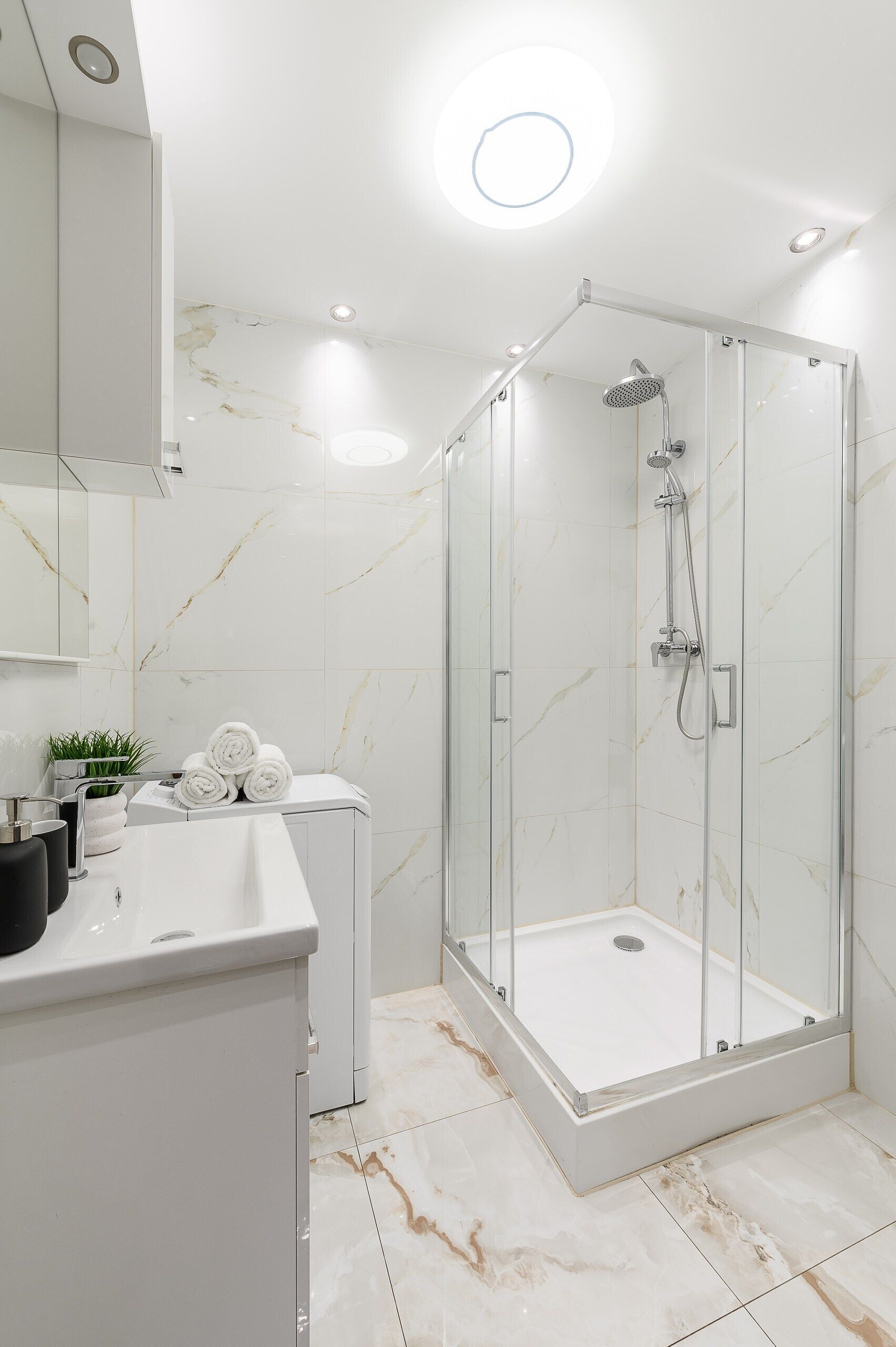 Ein modernes Badezimmer mit einer Glaskabine zur Dusche, einem weißen Waschtisch und Marmorfliesen.