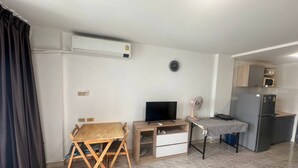 Un espacio habitable compacto con kitchenette, una zona de comedor con mesa y sillas, un televisor y una pequeña mesa con mantel a cuadros.