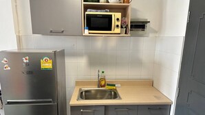 Una cocina compacta con un refrigerador de acero inoxidable, un microondas, un lavamanos y una encimera de madera.