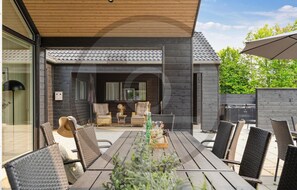 An outdoor patio with a wooden table and wicker chairs, a grill, and a covered seating area. - Amazing home in Bogense with sauna (Bogense)