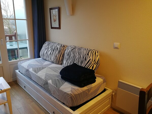 Una cama con cubrecama estampado de cebra, una mesita pequeña, un radiador y una ventana con vistas al exterior.