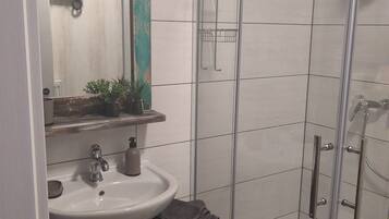 A bathroom with a sink, mirror, towel rack, and a glass-enclosed shower area.