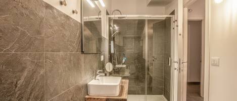 Un baño moderno con ducha de vidrio, lavamanos con encimera de madera y espejo sobre el lavamanos.