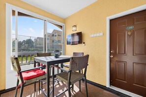 A balcony with a table and chairs, a door with a number plate, and a TV mounted on the wall.
