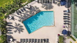 Vista aérea de uma área de piscina com espreguiçadeiras, guarda-sóis e palmeiras.