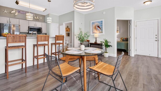 Cozinha moderna com eletrodomésticos embutidos, área de jantar com mesa redonda e cadeiras, e corredor com porta.