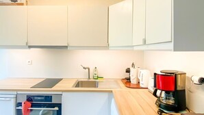 Una cocina moderna con armarios blancos, horno empotrado, cafetera y fregadero.
