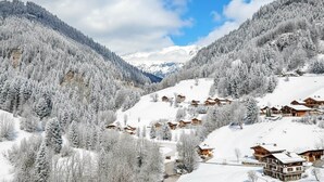 Un pueblo nevado en la montaña con chalets de madera, cielo despejado y un valle.