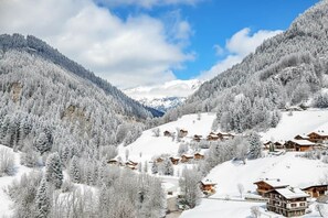 Ein verschneites Bergdorf mit Holzhäusern, klarem Himmel und einem Tal.