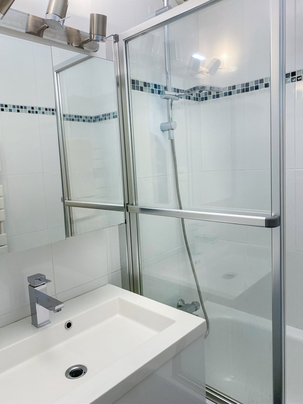 A modern bathroom with a glass shower enclosure, a white sink, and a tiled backsplash.