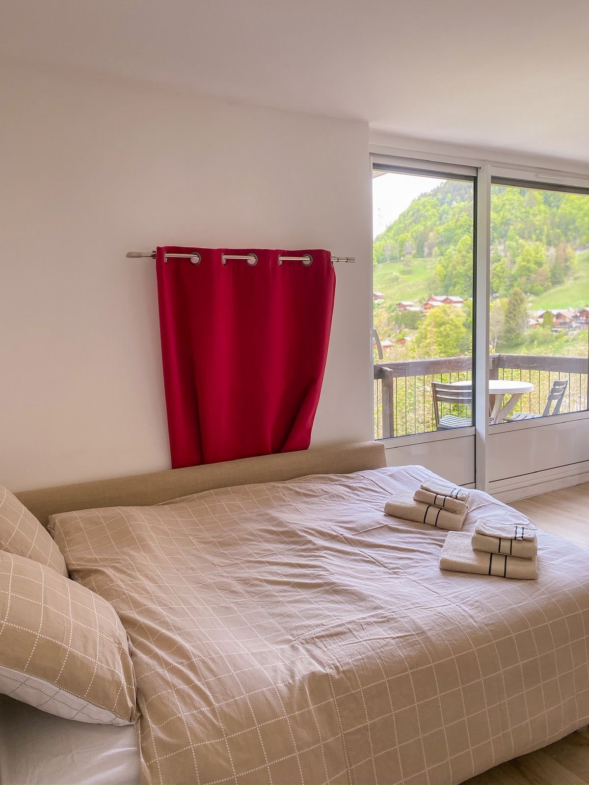 Una camera da letto con un letto, tende rosse e vista su un balcone con paesaggio esterno.