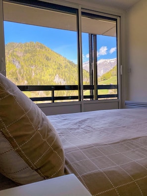 Ein Schlafzimmer mit einem Bett, einem Kissen und Blick auf eine Berglandschaft durch eine Schiebetür.