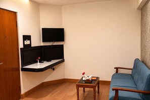 Una sala de estar con un sofá azul, una mesita de madera con un florero, un televisor de pantalla plana montado en la pared y una puerta de madera.