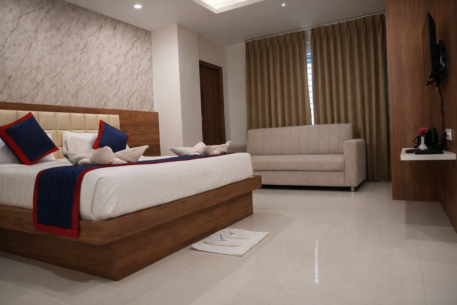 Een moderne slaapkamer met een groot bed, een sofa, een flatscreen televisie en een houten accentmuur.