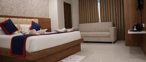 A modern bedroom with a large bed, a sofa, a flat-screen TV, and a wooden accent wall.
