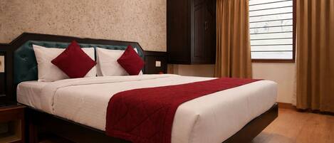 A hotel room with a large bed, dark wooden headboard, and a window with curtains.