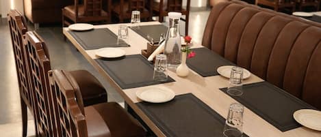 A restaurant with a long table set for dining, booths, and a bar area.