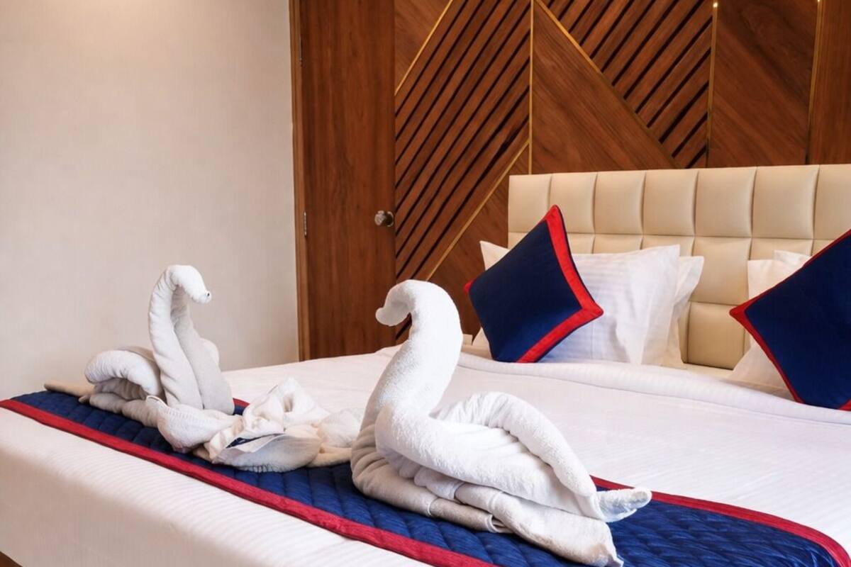 Una habitación de hotel con una cama, un cabecero de madera y dos toallas con forma de cisne sobre la cama.