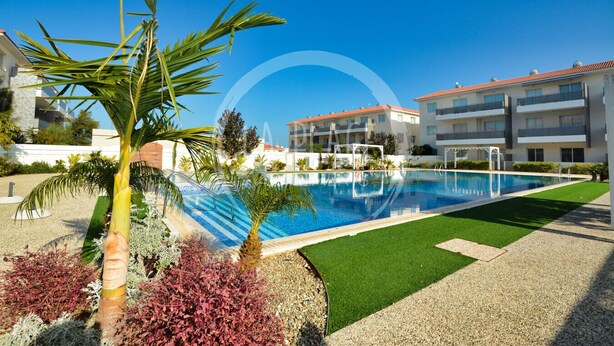 A swimming pool with a clear blue water, surrounded by a well-maintained lawn and palm trees. - Cosy 2Br Family Apartment - Mythical Sands Resort (Paralimni)