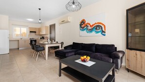Een modern appartement met een eethoek, een zwarte bank en een keuken op de achtergrond.