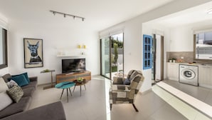 A modern living room with a flat-screen TV, a sofa, a coffee table, and a patterned armchair. - Stylish Villa | Private Pool - Garden - Near Beach (Paralimni)