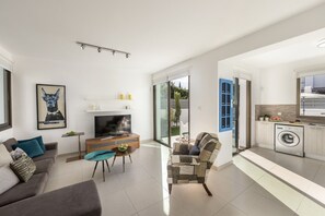 Een moderne woonkamer met een flatscreen televisie, een bank, een salontafel en een fauteuil met een patroon.