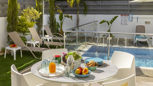 A poolside area with a table set for breakfast, lounge chairs, and a glass railing overlooking the pool. - Stylish Villa | Private Pool - Garden - Near Beach (Paralimni)